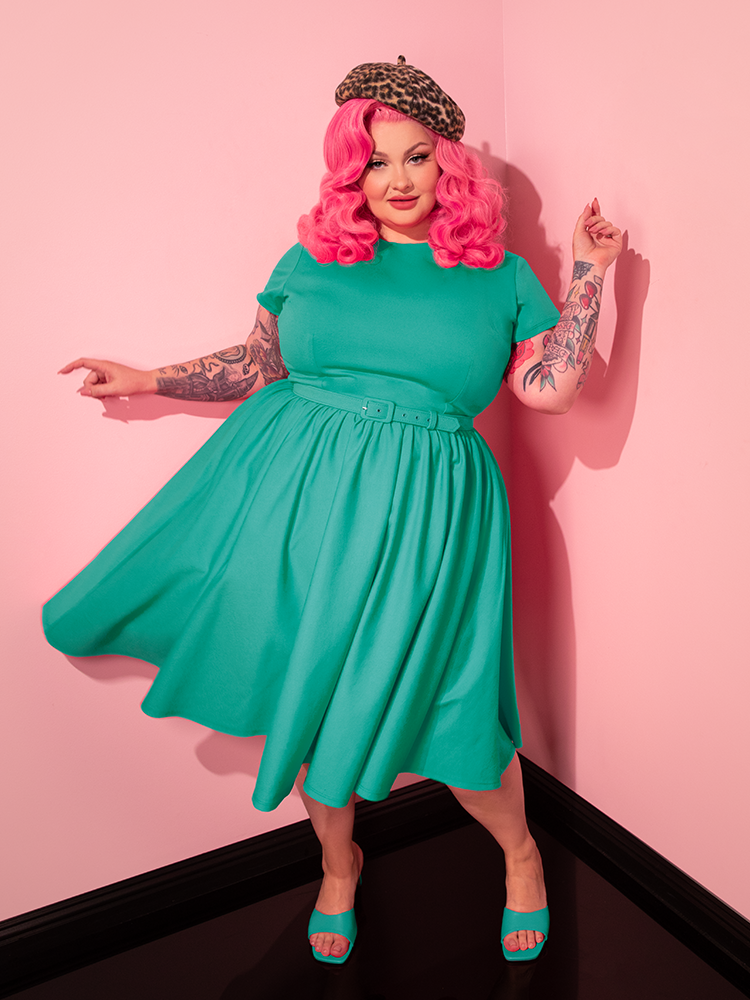 With every movement, the female model brings the Avon Swing Dress in Aquamarine to life, embodying the essence of retro glamour by Vixen Clothing.
