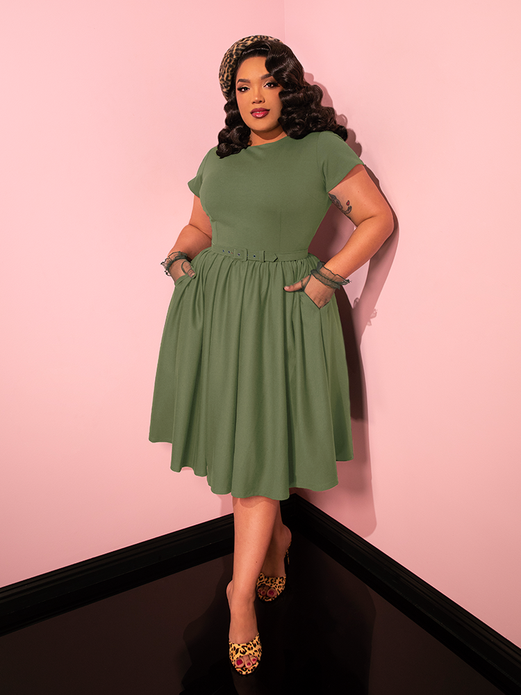 Radiating elegance, the female model demonstrates the timeless charm of the Avon Swing Dress in Sage Green from Vixen Clothing through a variety of poses.