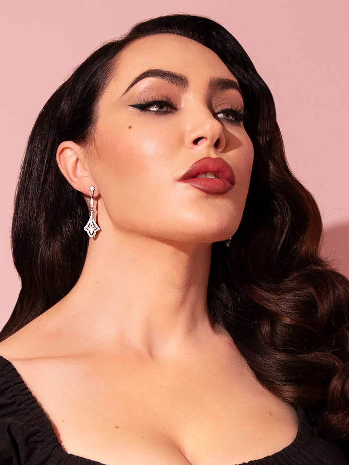 Micheline Pitt exudes timeless elegance as she graces the scene, showcasing the Art Deco Dangle Rhinestone Earrings from the retro clothing brand Vixen Clothing, adding a touch of vintage glamour to her impeccable style.
