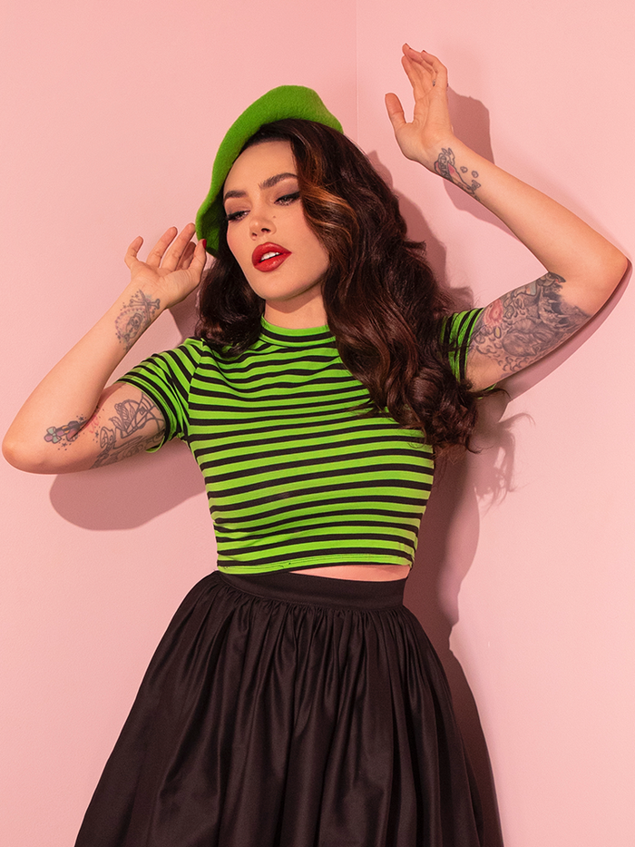 Wearing the Bad Girl Crop Top in Slime Green and Black Stripes, Micheline Pitt strikes a pose for the camera, representing the retro charm of Vixen Clothing.