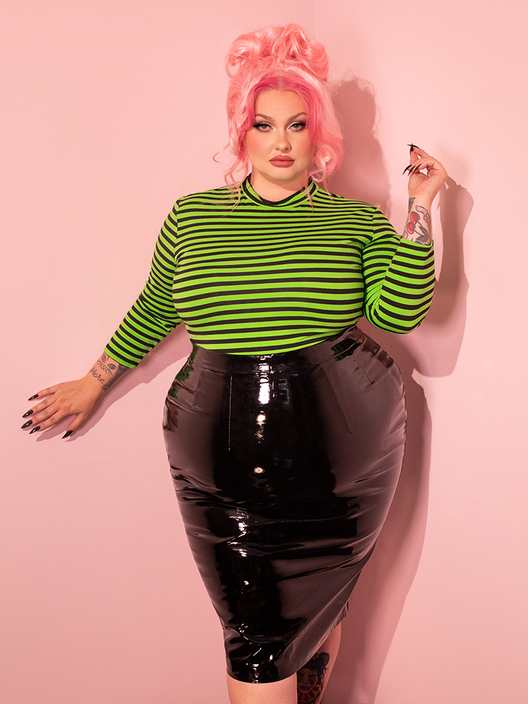Witness the beauty of a female model as she showcases the Bad Girl 3/4 Sleeve Top in Vibrant Slime Green and Black Stripes from the renowned retro brand, Vixen Clothing.