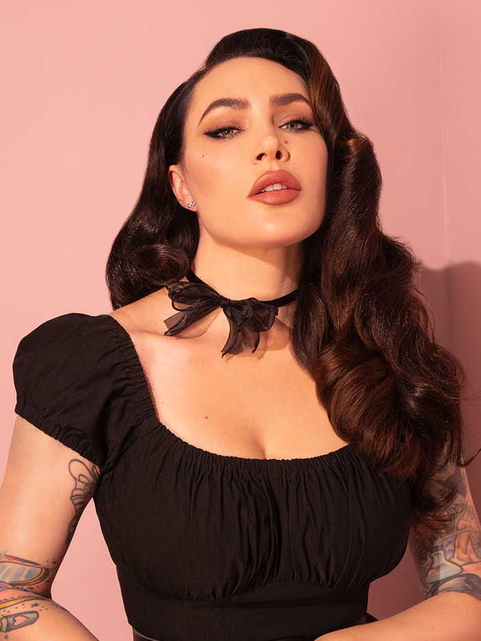 Micheline Pitt elegantly dons the Black Velvet Choker adorned with a charming bow from the iconic retro fashion brand, Vixen Clothing.