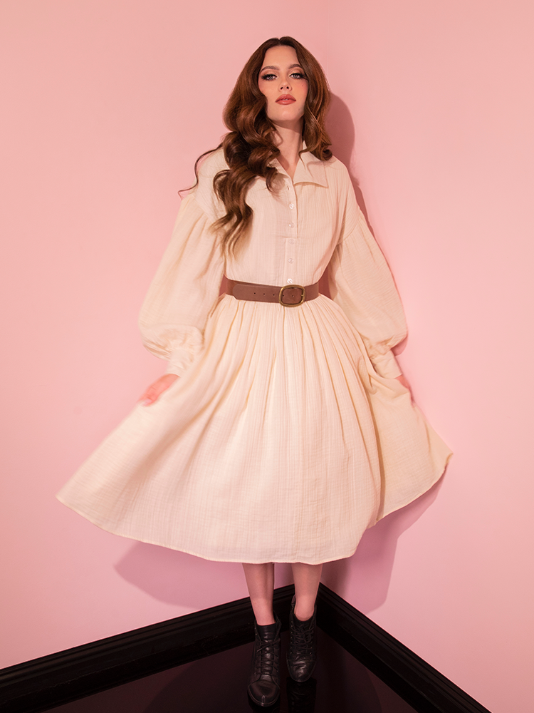 Embrace elegance with the Cream Fantasy Shirtdress and its Faux Leather Belt, artfully presented by our retro-inspired model, courtesy of Vixen Clothing.