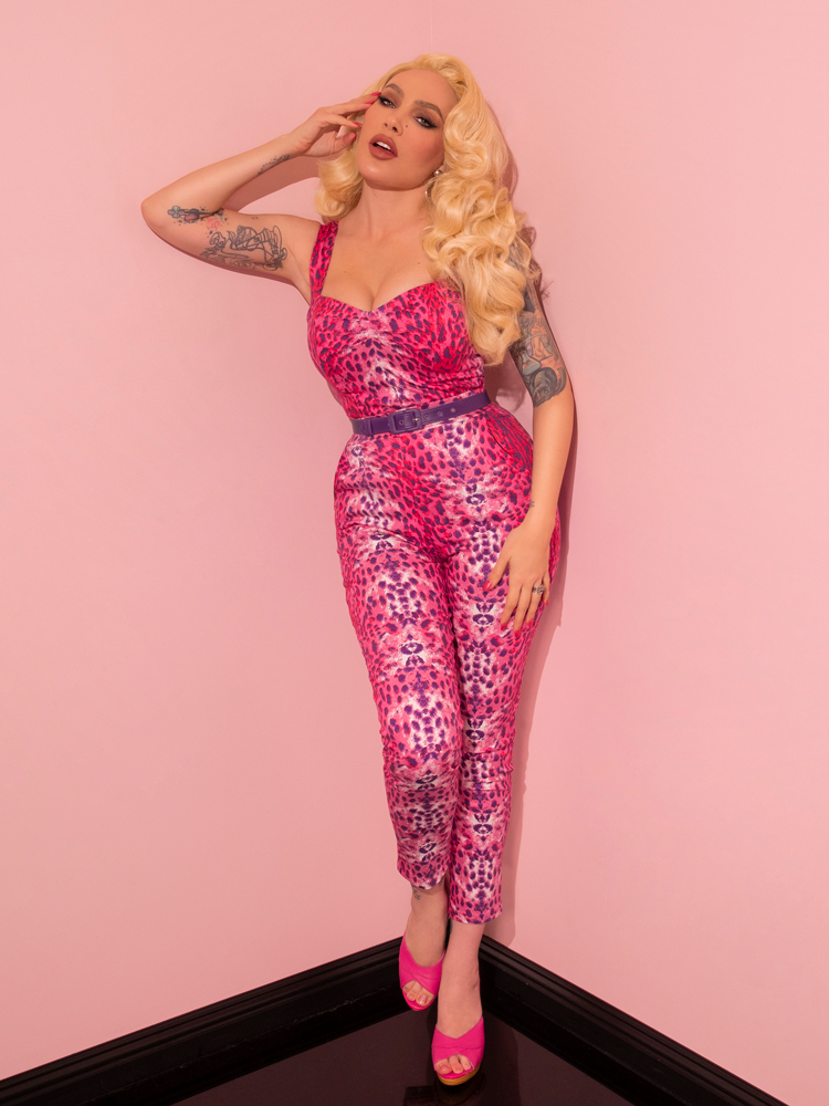 Embodying retro chic, a lovely female model captivates with her stylish demeanor while wearing the Pink Leopard Print Cigarette Pants from Vixen Clothing, a brand that specializes in vintage clothing.