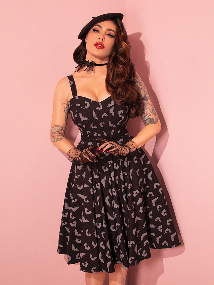 Behold the elegance of a stunning female model dressed in the Maneater Swing Dress, featuring the Glow in the Dark Bat Print in Black, by the retro dress brand Vixen Clothing.