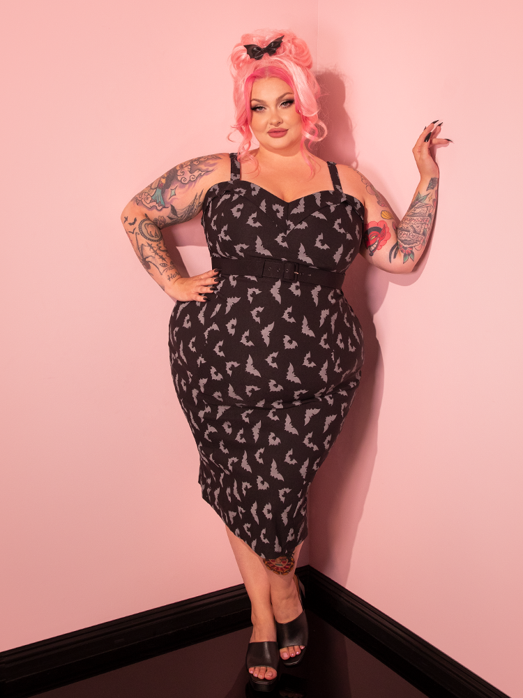 Witness the beauty of our impeccably styled model as she confidently displays the Maneater Wiggle Dress in Black Glow in the Dark Bat Print, courtesy of Vixen Clothing, the premier retro dress and clothing brand.