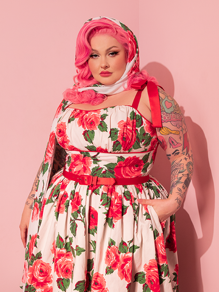 The stunning retro-clad lady model impeccably matches her vintage-style dress, embellished with a charming red rose pattern, with the 1950s-inspired Chiffon Rose Scarf by Vixen Clothing, adding a timeless touch to her ensemble.