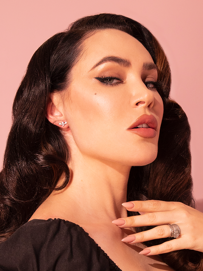 An enchanting female model is elegantly adorned with the Tiny Rhinestone Bat Stud Earrings in Silver, a creation of the vintage fashion brand Vixen Clothing.