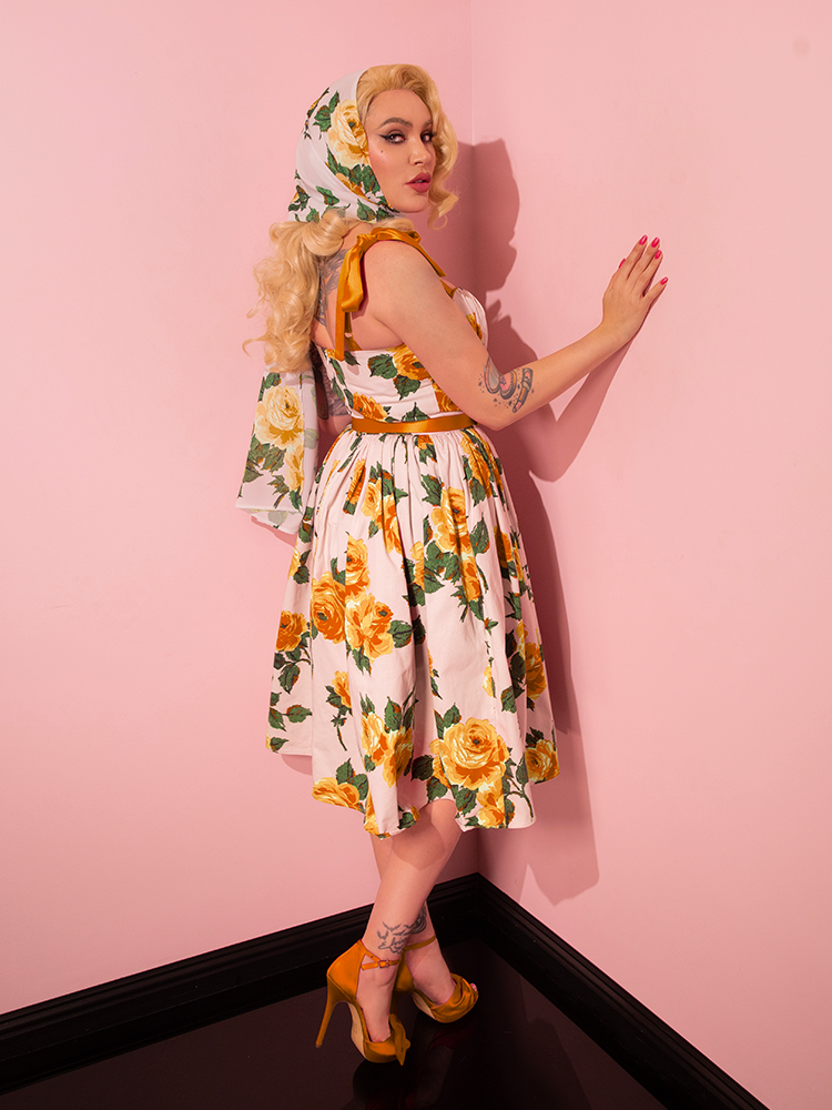 Displaying versatility, Micheline Pitt models the 1950s Swing Sundress and Scarf in Yellow Vintage Roses from Vixen Clothing, striking a variety of captivating poses.