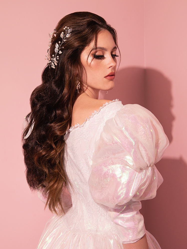 Prepare to be enchanted by the ethereal beauty of the very limited edition Pearlescent White LABYRINTH™ Sarah Goblin Ball Gown, magnificently showcased by a captivating mannequin from the retro archives of Vixen Clothing.