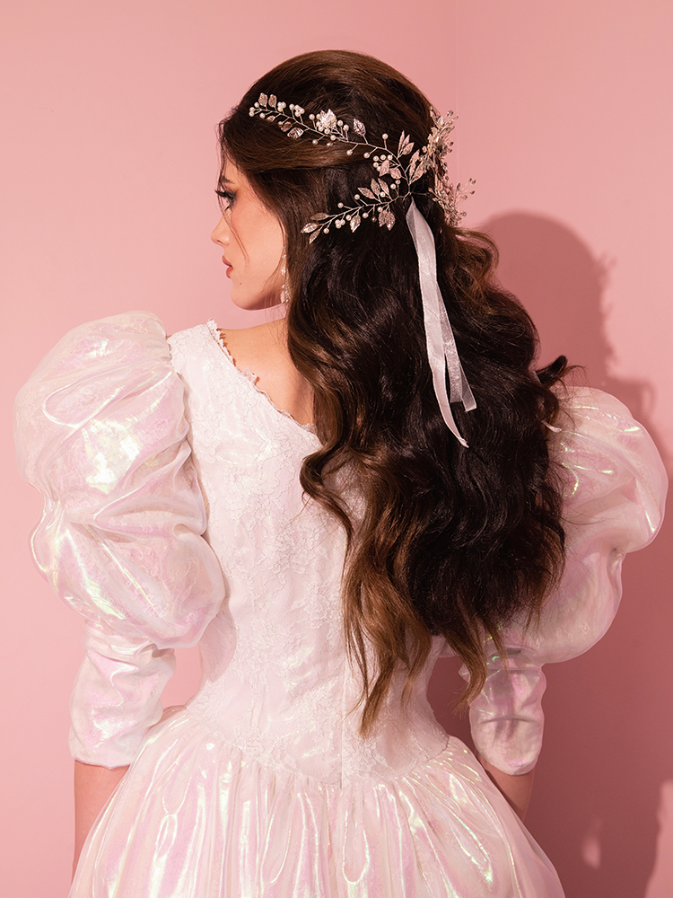 A vision of retro sophistication comes to life with the LABYRINTH™ Sarah Goblin Ball Gown in Pearlescent White, gracefully worn by a charming lady from the illustrious Vixen Clothing, the ultimate vintage curator.
