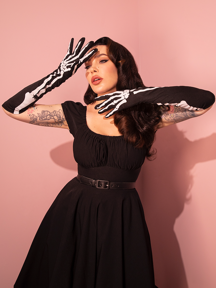 Micheline Pitt, a true retro fashion icon, models the iconic Skeleton Print Full-length Opera Gloves by Vixen Clothing, elevating her outfit with vintage flair.