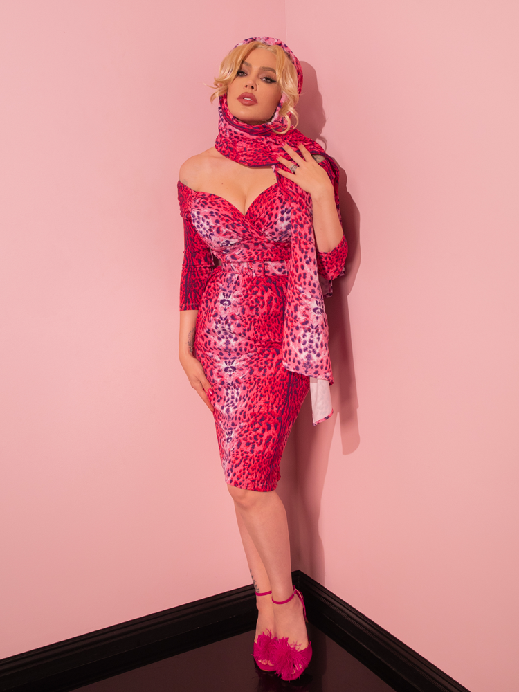 Behold the exquisite beauty of a retro-inspired female model, gracefully showcasing the Pink Leopard Print Starlet Wiggle Dress and Scarf by the renowned Vixen Clothing, evoking the essence of the past.