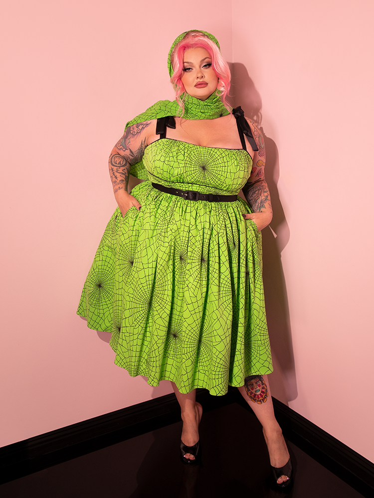 Witness the beauty of a female model as she dons the 1950s Swing Sundress and Scarf in Vibrant Slime Green Spider Web Print, brought to you by the renowned retro brand, Vixen Clothing.