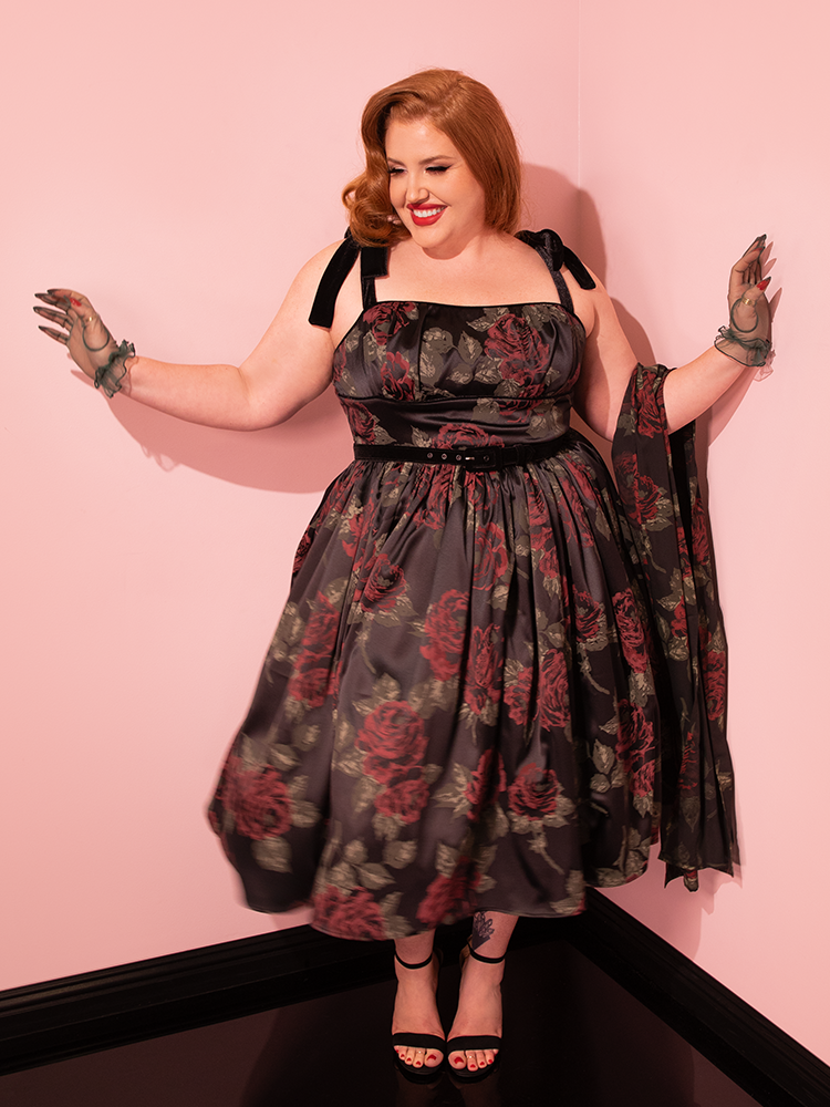 Embrace the vintage glamour with Vixen Clothing's 1950s Satin Swing Sundress and Scarf in Black Vintage Roses. Witness the captivating presence of vintage models as they showcase this classic piece with timeless charm.