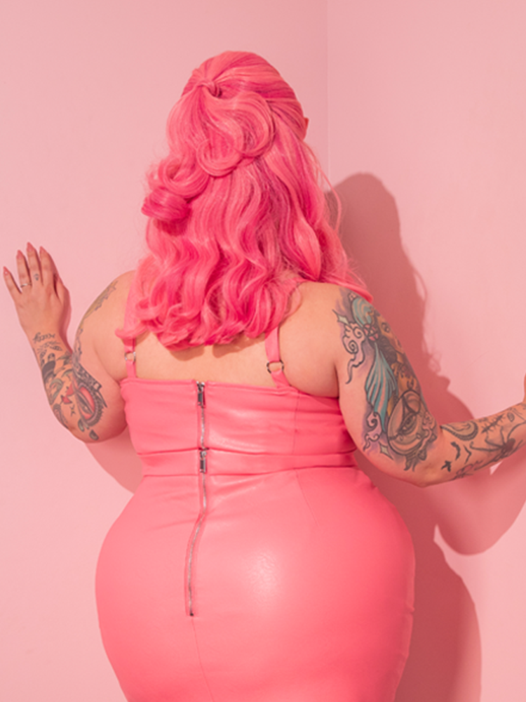 Experience a blast from the past as the breathtaking model showcases the exclusive Bad Girl Maneater Top in Flamingo Pink Vegan Leather, a true relic from the retro dress and vintage clothing aficionados, Vixen Clothing.