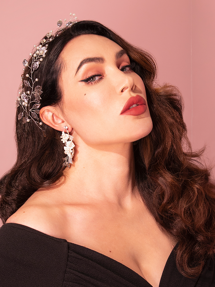 The Vintage-Style Leaf and Pearl Hair Wire in Silver from Vixen Clothing, a distinguished retro brand, is showcased by an attractive brunette model in a playful and charming pose.