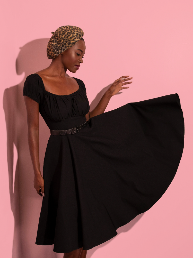 The skirt section of the Peasant Swing Dress in Black flies out while a model poses in the all new retro dress offering from Vixen Clothing.
