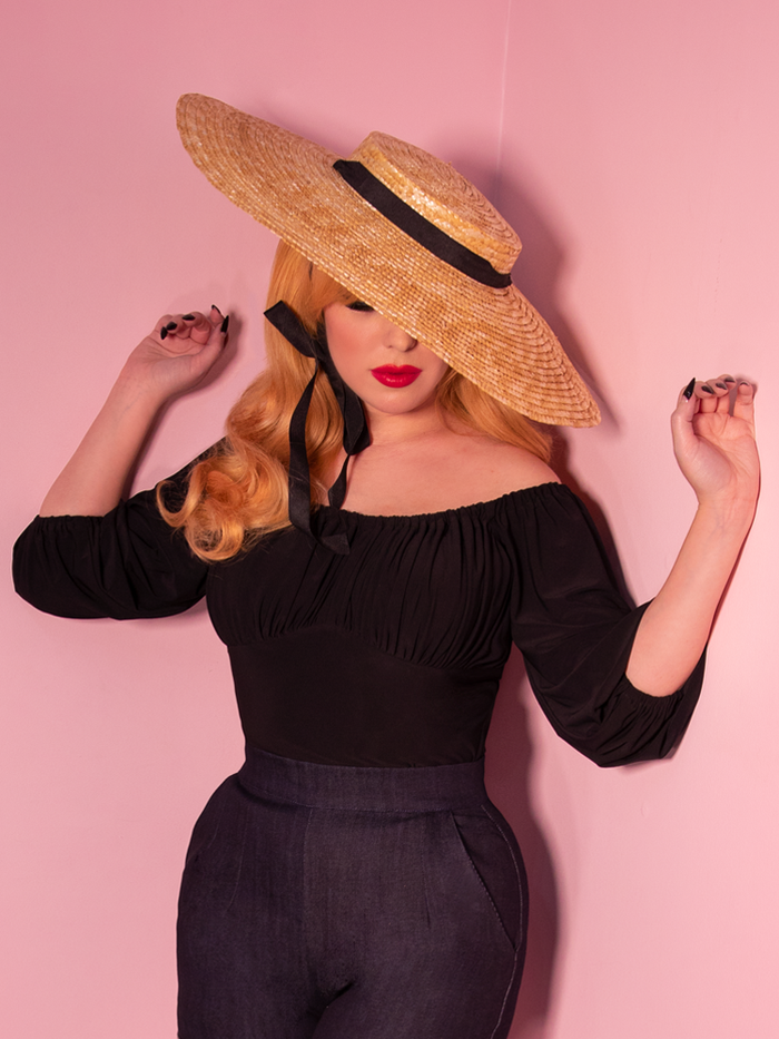 Black vacation blouse worn by blonde model wearing sunhat.
