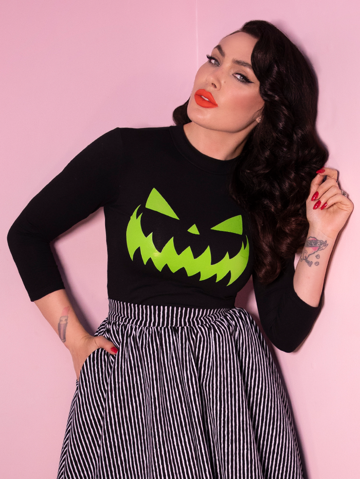 Close shot of Micheline Pitt wearing the Black Pumpkin King 3/4 length shirt from Vixen Clothing. It features an original jack-o-lantern design on the front and has 3/4 sleeves.