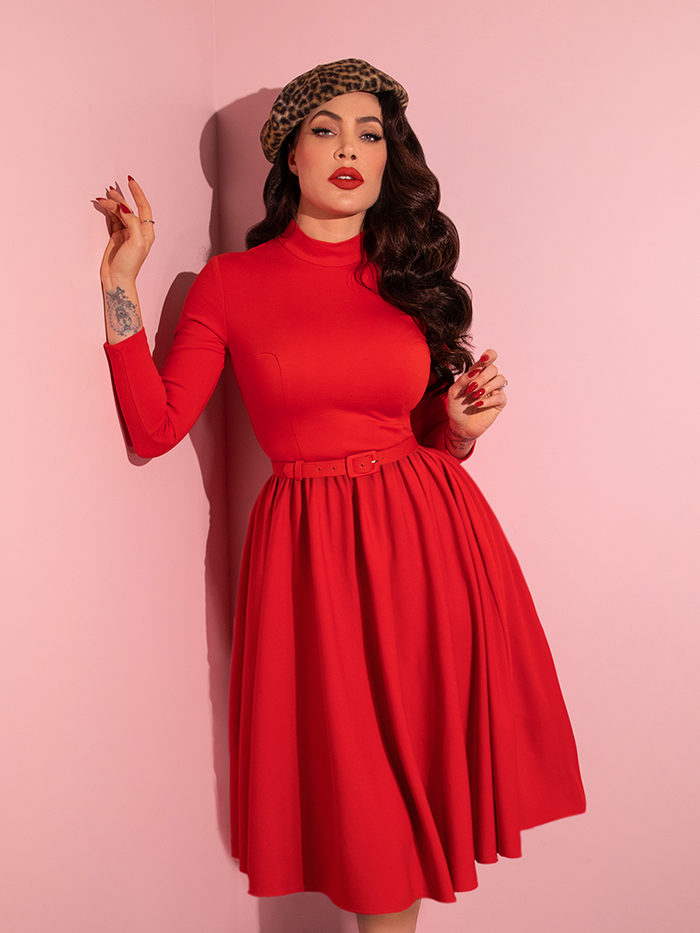 Micheline Pitt poses in the Bad Girl Swing Dress in Tomato Red while also wearing a leopard print beret. 