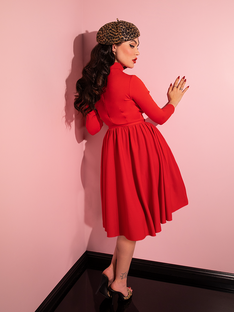 Micheline Pitt turned away from the camera but subtly looking back over her shoulder wears the Bad Girl Swing Dress in Tomato Red.