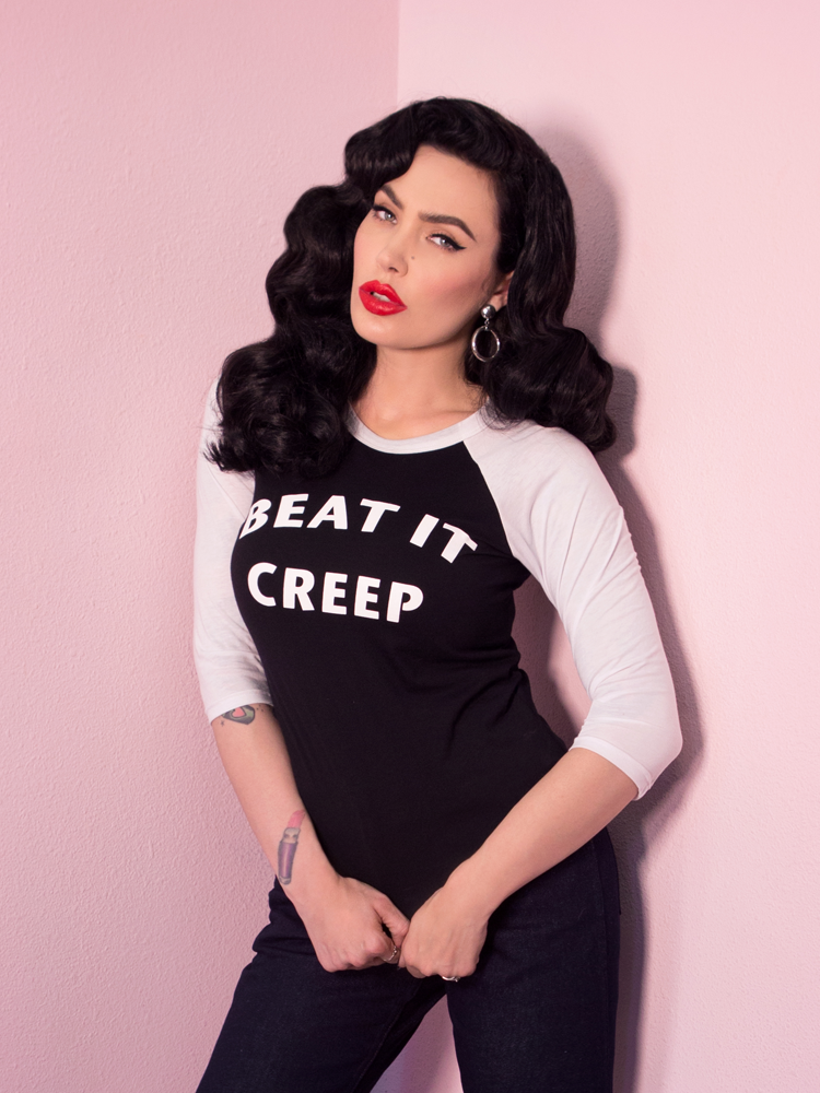Micheline Pitt looking at the camera while modeling the Beat It Creep raglan t-shirt by Vixen Clothing.