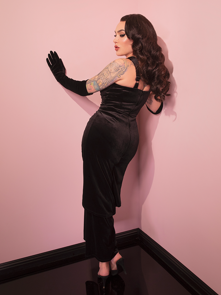 Micheline Pitt turned away from the camera to show off the back of the Golden Era Gown and Glove Set in Black Velvet from Vixen Clothing.