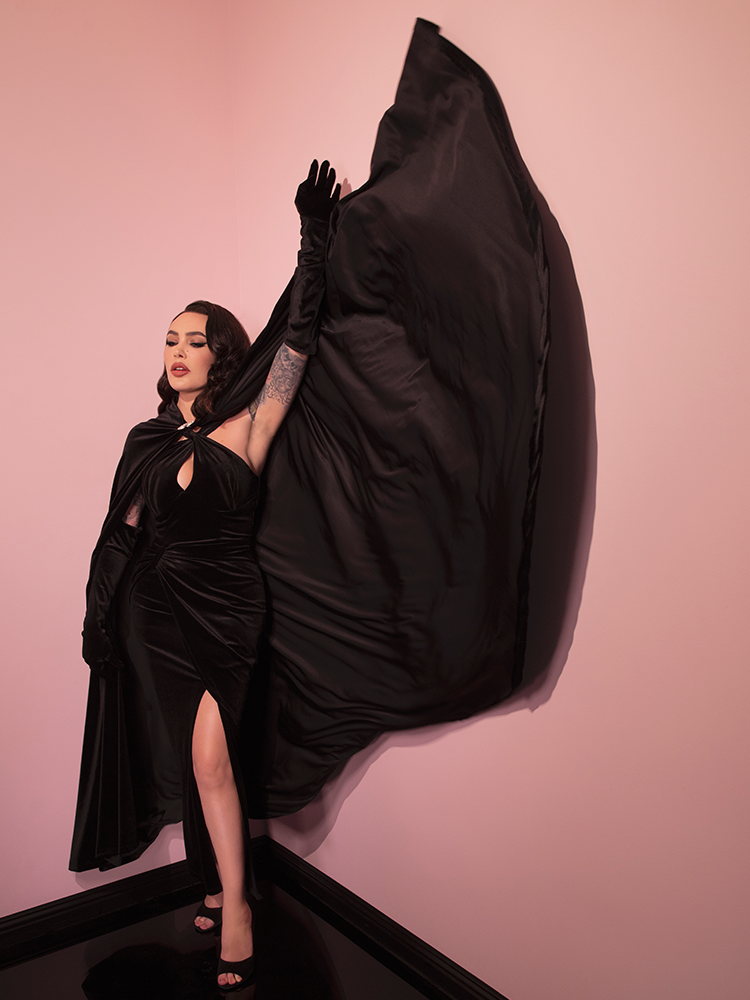Micheline Pitt throws back her black cape that matches perfectly with the Golden Era Gown and Glove Set in Black Velvet. All items available from Vixen Clothing.