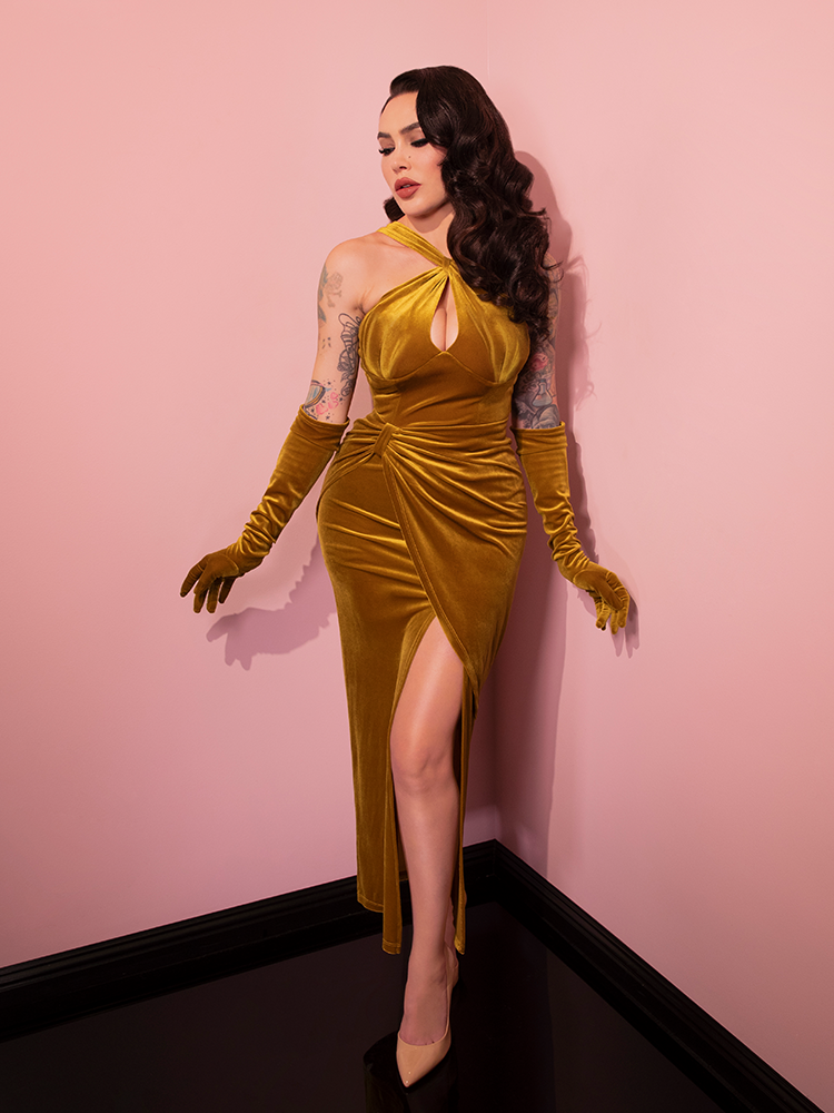 Micheline is looking down with her arms to the side in a pink room while wearing the Golden Era gown and glove set.