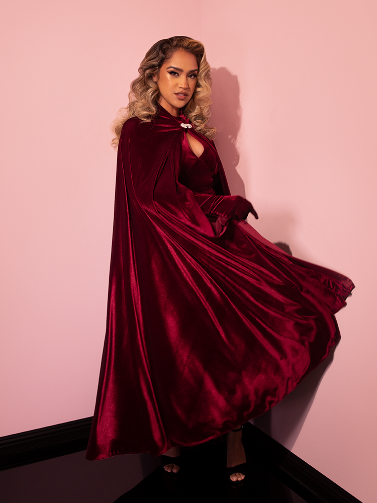 Female model swings the Golden Era Cape in Burgundy Velvet Around to show off the luxurious velvet fabric. 