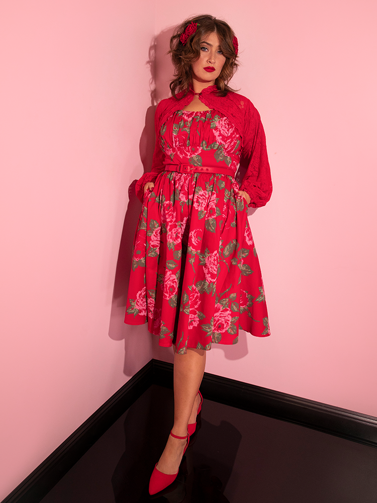 Francesca strikes a cool pose with both hands tucked into the pockets of her Ingenue Swing Dress in Vintage Red Rose Print from Vixen Clothing.