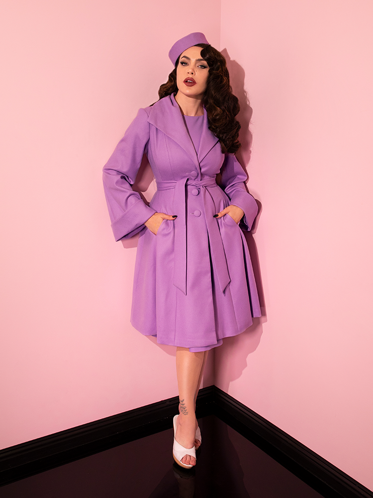Full length shot of Micheline Pitt wearing a ravishing retro clothing outfit highlighted by the The Lili Coat in Lilac.