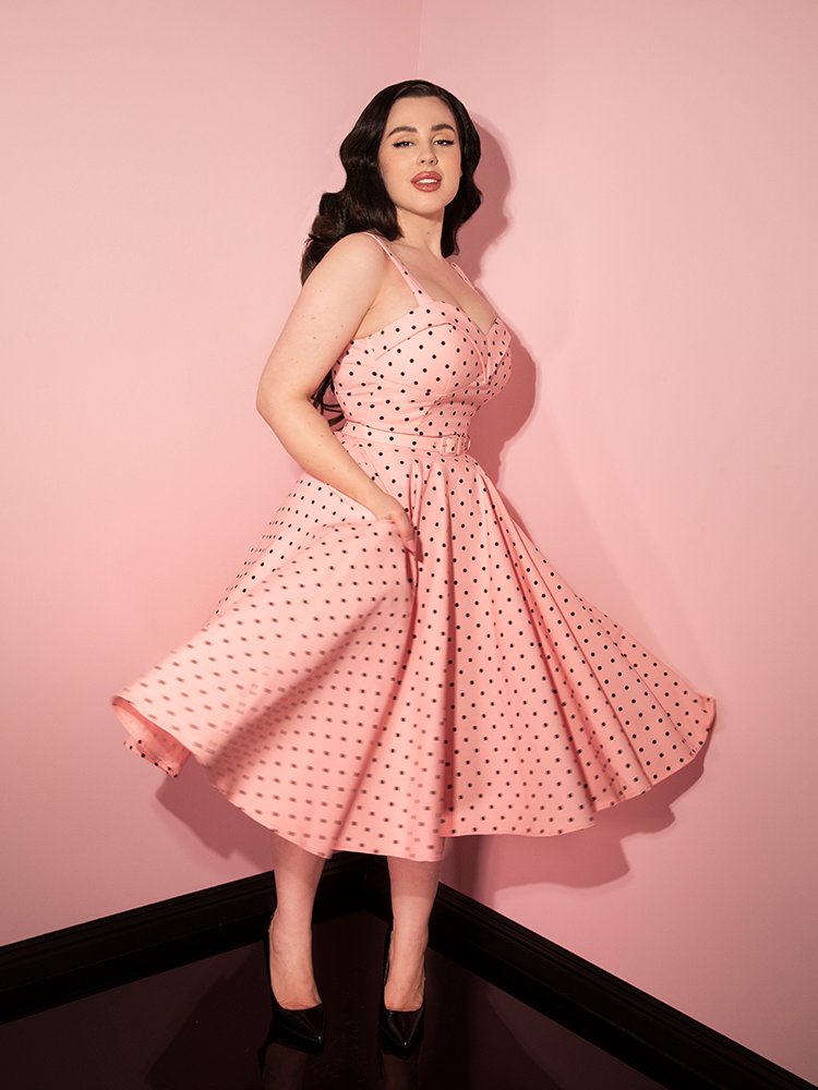 Rachel Sedory caught mid-twirl in the Maneater Swing Dress in Rose Pink Polka Dot with her hands placed in the hidden pockets of the dress.