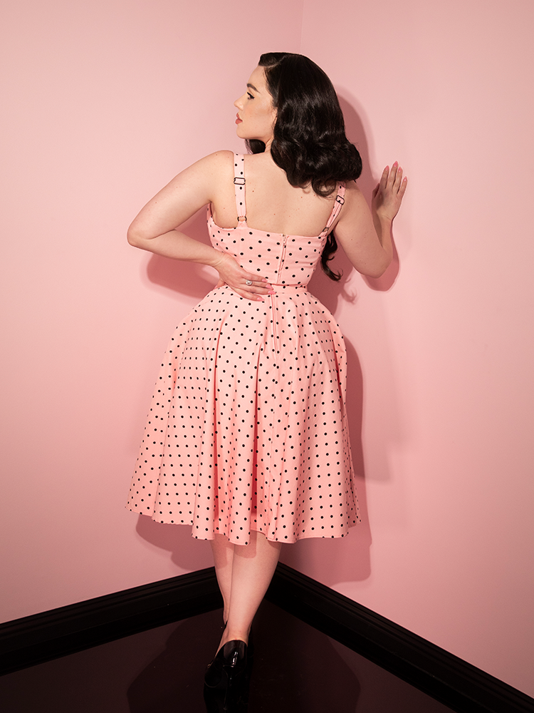 Rachel Sedory faces away from the camera while looking back slightly in the Maneater Swing Dress in Rose Pink Polka Dot.