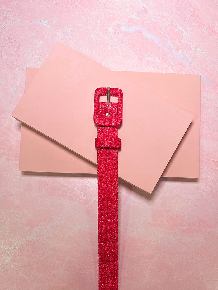 The 1" Belt in Candy Pink Lurex photographed on a pink stone surface. 