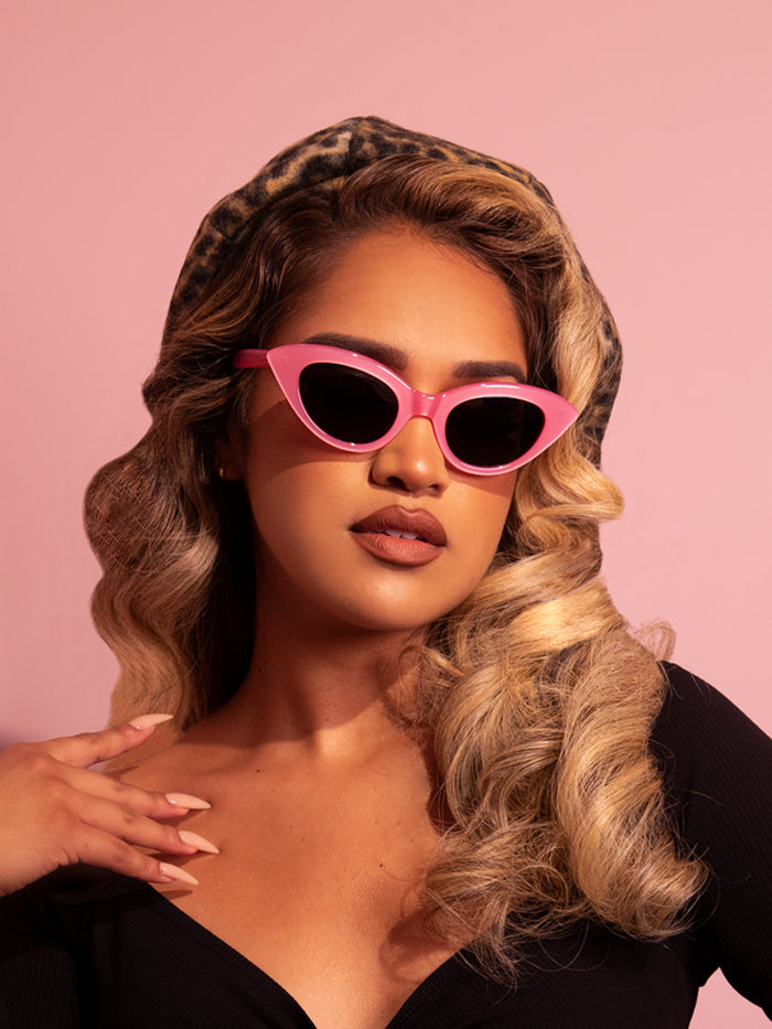 Tan female model shows off the Fashion Doll Cat Eye Sunglasses in Pink from vintage clothing brand Vixen Clothing.