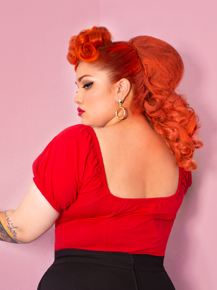 A back shot of Evelyn looking over her shoulder modeling the Powder Puff top in red by Vixen Clothing.