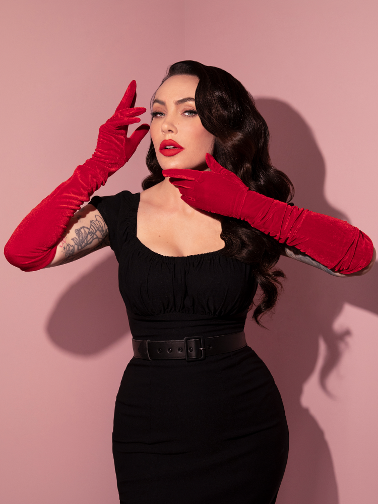 Micheline Pitt wears a form fitting black retro style dress that is accented brilliantly by her Velvet Gloves in Red. 