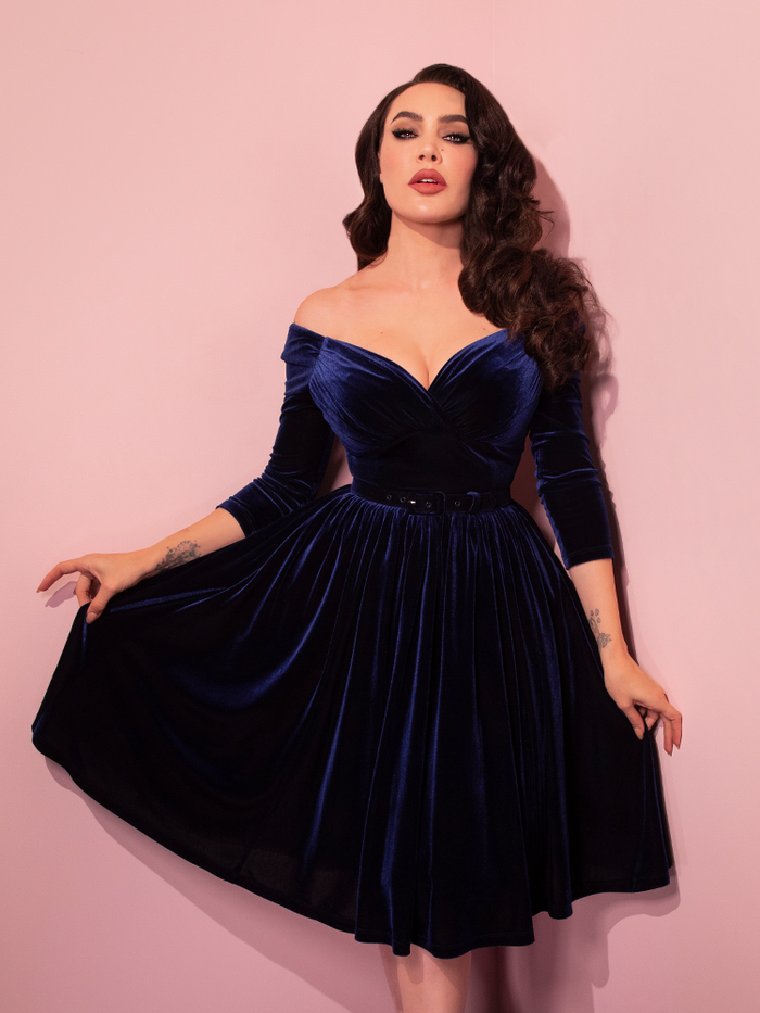 Micheline Pitt photographed looking directly into the camera while modeling the Starlet Swing Dress in Navy Velvet from retro dress brand Vixen Clothing.