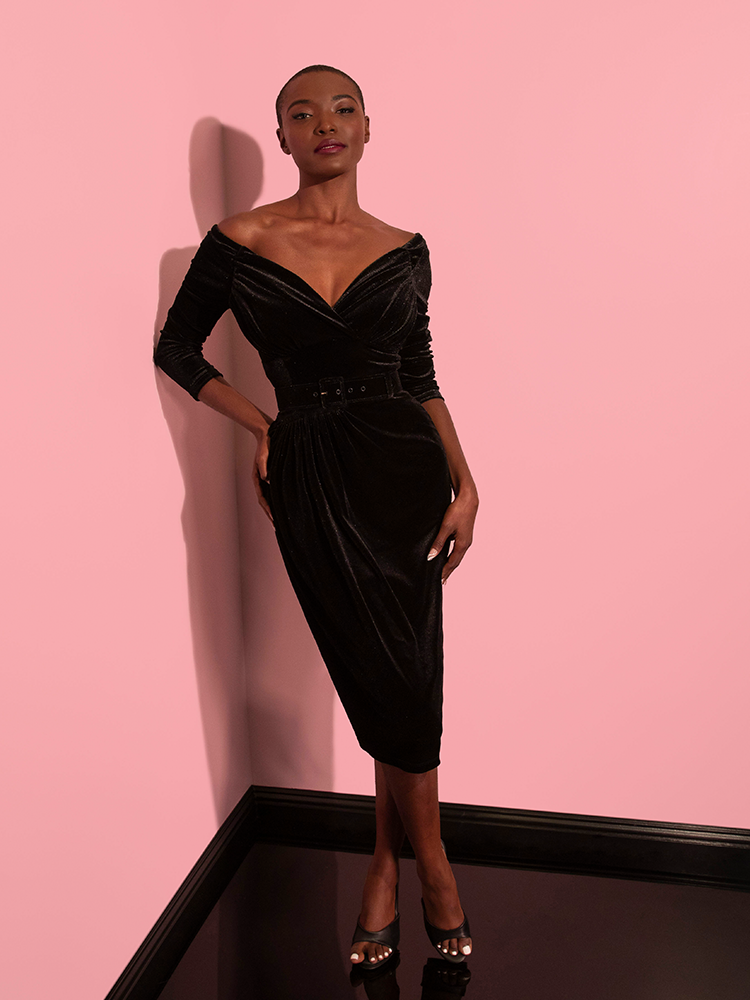 The Starlet Wiggle Dress in Black Velvet from Vixen Clothing looks phenomenal on the female model, who showcases the dress's beauty with every movement.