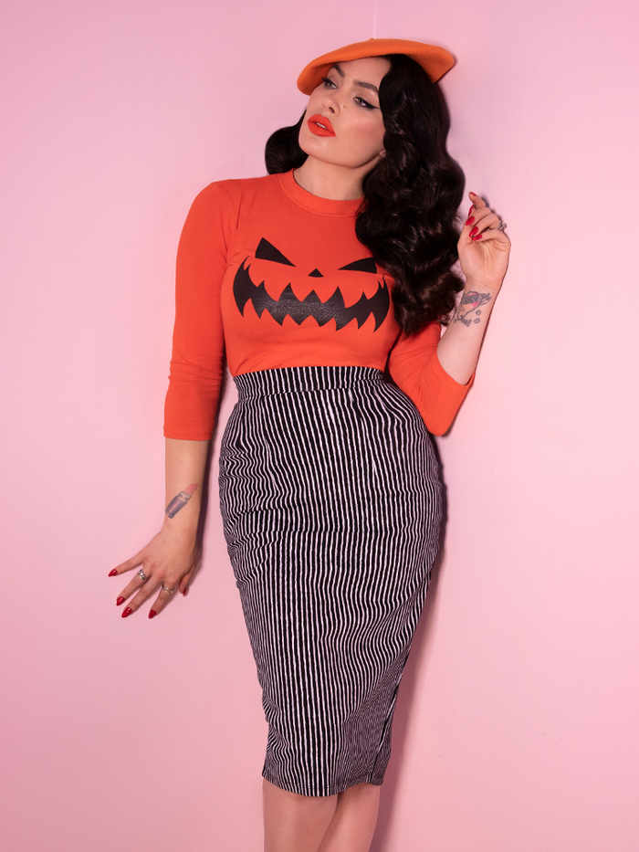 Model and owner Micheline Pitt wears the Vixen Pencil Skirt in Black and White Stripes along with an orange long sleeve top with classic pumpkin face design.