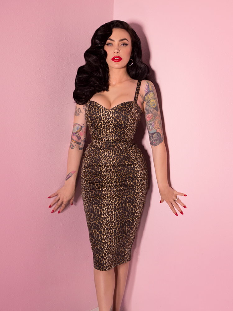 Micheline Pitt wearing a leopard print wiggle dress standing against a pink background.