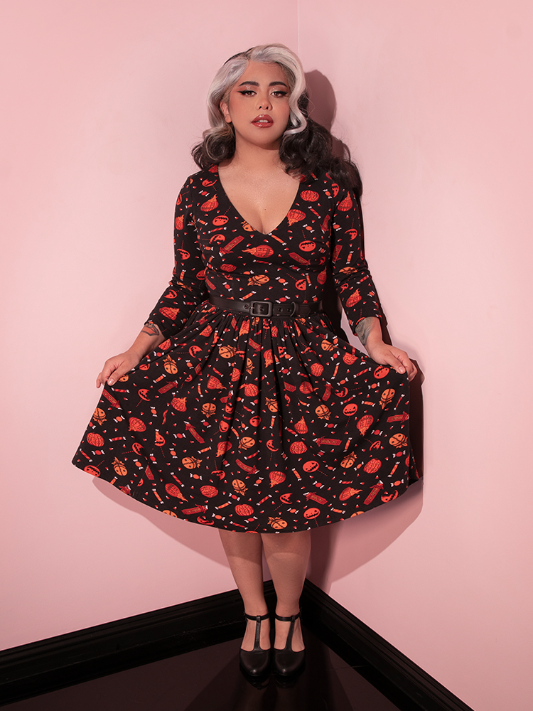 Model posing in the corner of her room while wearing the TRICK R TREAT™ Deadly Swing Dress in Candy Corn Novelty Print.