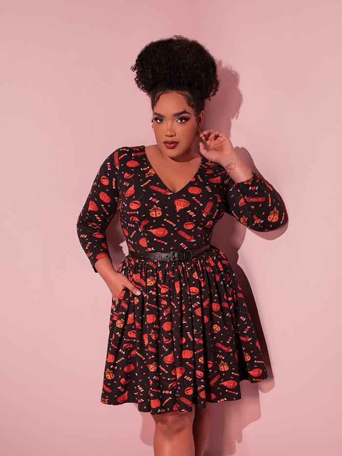 Model poses with one hand tucked into the pocket on the TRICK R TREAT™ Deadly Swing Dress in Candy Corn Novelty Print.