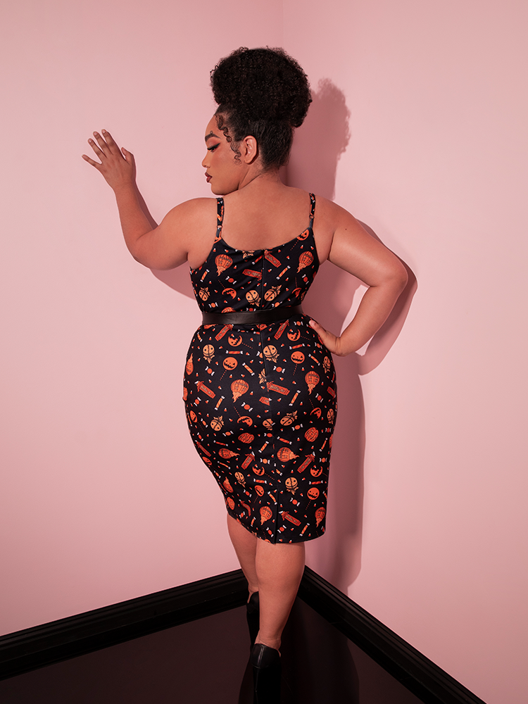 The back of the TRICK R TREAT™ Peplum Wiggle Dress in Candy Corn Novelty Print modeled by a female model while also wearing a black vegan leather belt.