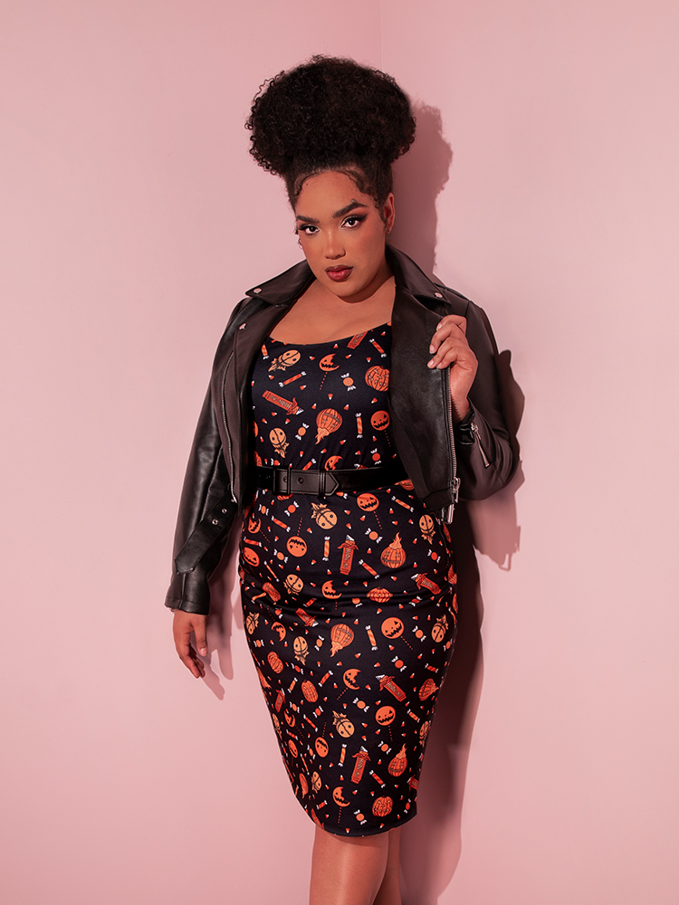 Female model wearing the TRICK R TREAT™ Peplum Wiggle Dress in Candy Corn Novelty Print with a black vegan leather.