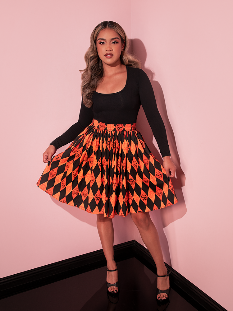 Model pulling out the sides of the TRICK R TREAT™ Skater Skirt in Halloween Harlequin Print along with a tucked in long-sleeve black top.
