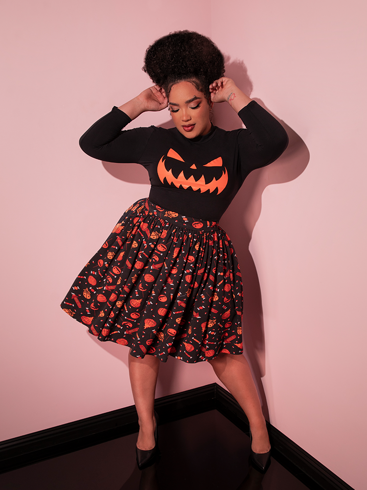 Model swings her hips around while wearing the TRICK R TREAT™ Skater Skirt in Candy Corn Novelty Print with black long-sleeve pumpkin shirt.