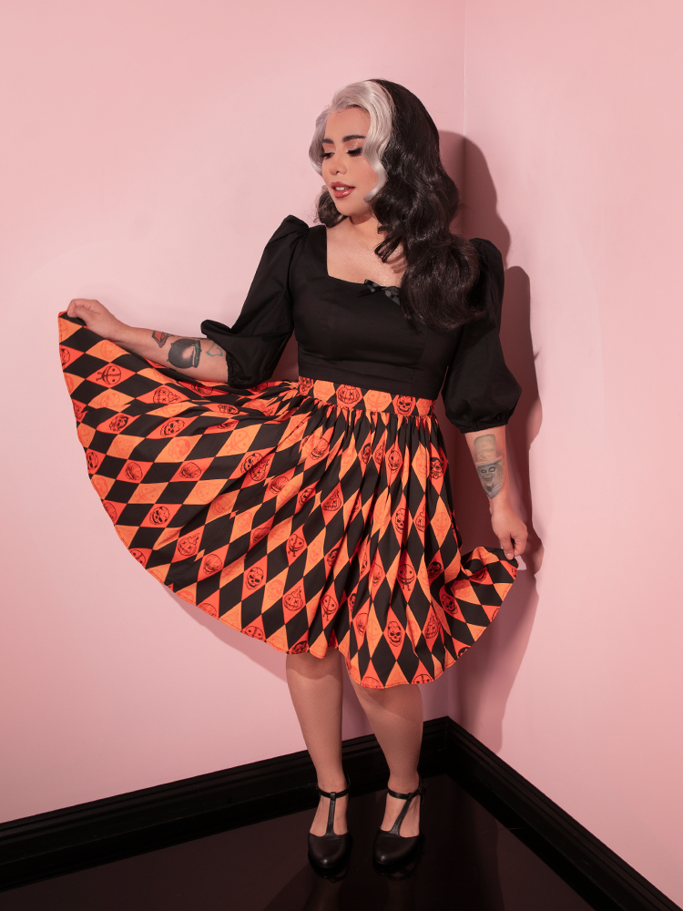 The TRICK R TREAT™ Skater Skirt in Halloween Harlequin Print being worn by female model along with a long sleeve black retro top.